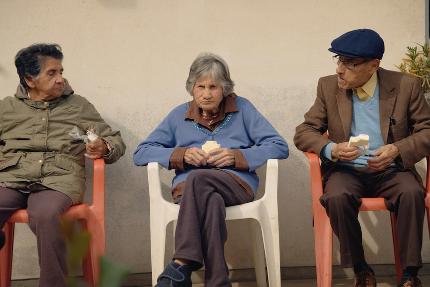 An elderly man, the spy Sergio Chamy, sitting outside next to two elderly women in documentary The Mole Agent