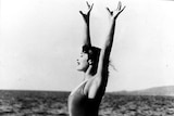 Annette Kellerman standing on a rock by the ocean with her hands up as if she's about to dive into the water