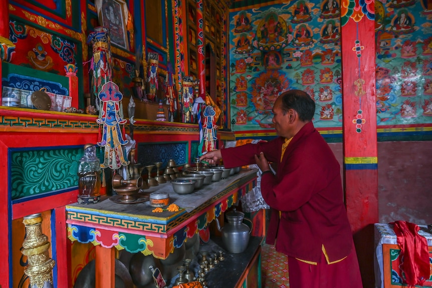 A man in maroon clothes places an offering in a silver dish on an alter