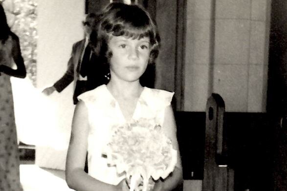 A scanned black and white photograph of a little girl walking down the aisel of a wedding chapel holding flowers