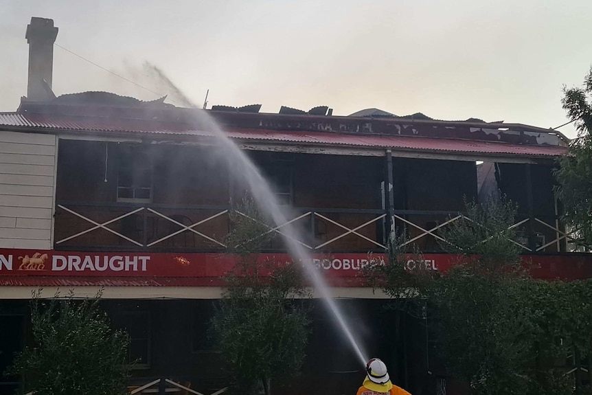 A firefighter aims a powerful stream of water from his house at the roof of an old pub.