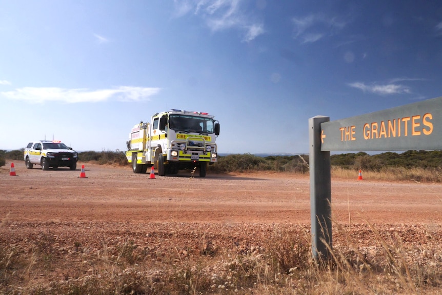 Emergency services vehicle parked at dirt road with green painted wooden sign on left in foreground saying The Granites