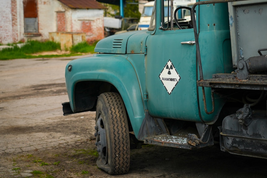 Ein Lastwagen mit einem platten Vorderreifen rechts parkte auf dem Dreck.  Auf die Tür ist ein radioaktives Symbol gemalt