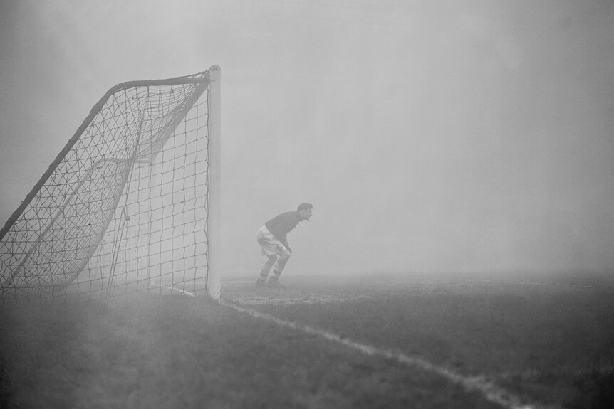 A goalkeeper stands in the fog next to a goal