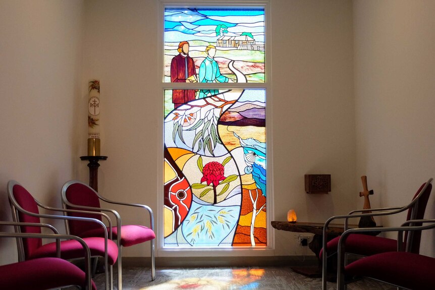 Religious room with stained Australiana-style glass windows and candle.