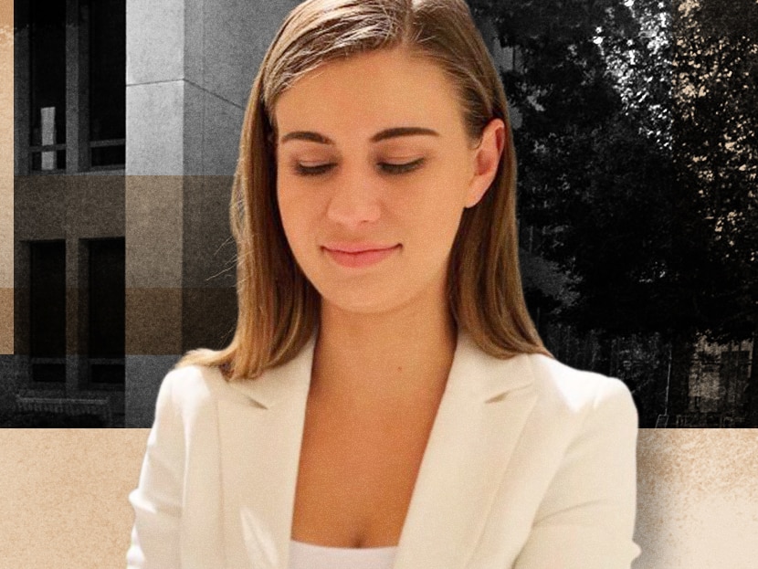 A young woman with long brown hair sits in a courtyard looking down wearing a white blazer and white top