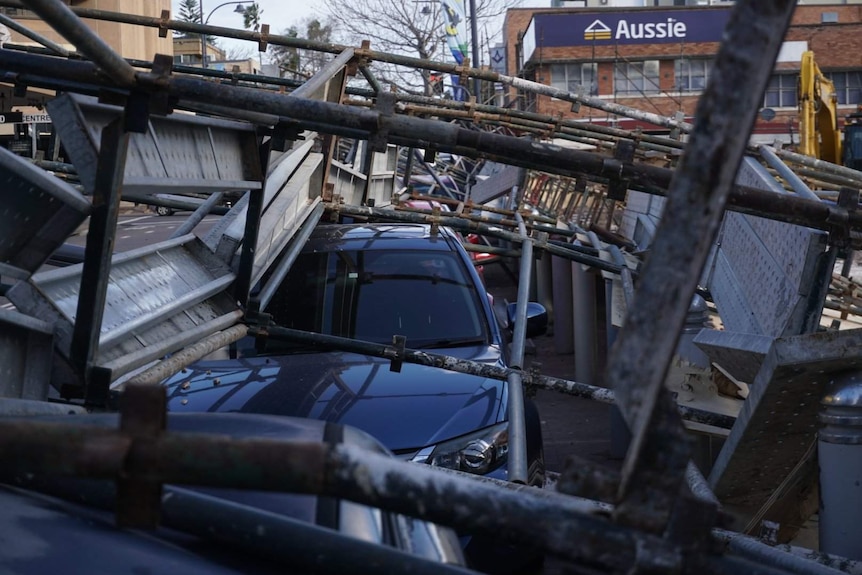 Collapsed scaffolding lies over a parked black car.