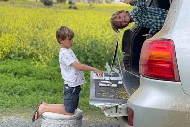 two young boys in the back of a ute parked in a paddock, one sits at the tailgate looking at a computer 