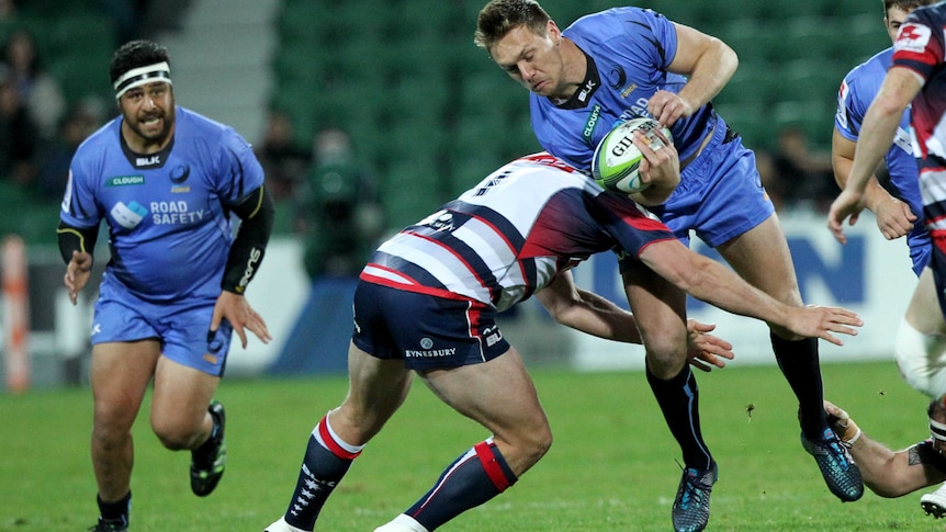 Western Force player  Dane Haylett-Petty is tackled from the side by a Melbourne Rebels player while carrying a rugby ball.
