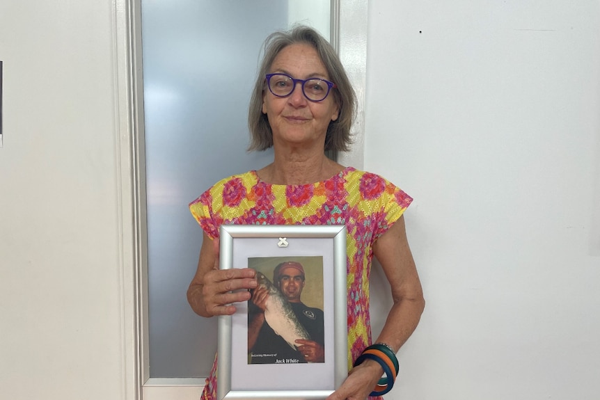 woman stands in front of wall holding picture in a frame 