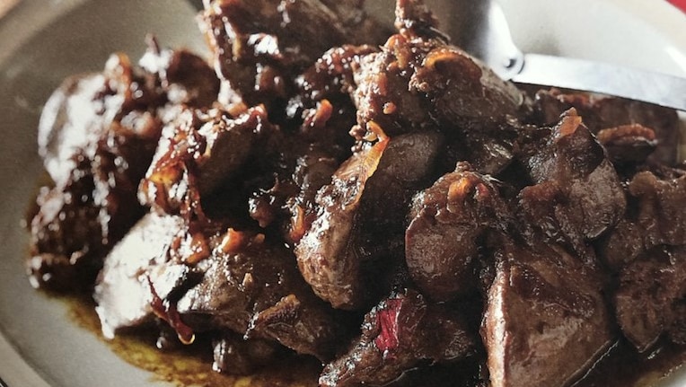 Browned livers with onions and a yellow oily sauce on a white plate with spoon.