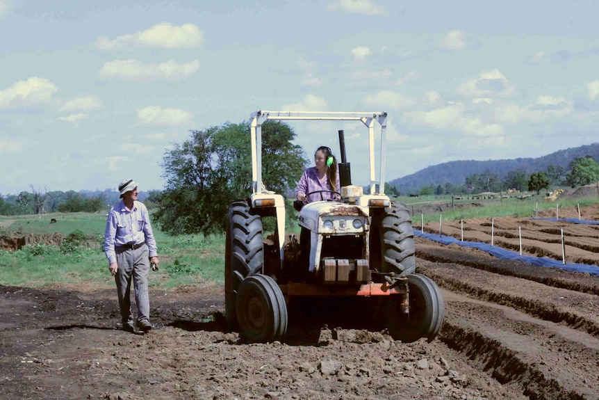 A woman driving a tractor looks at a man.
