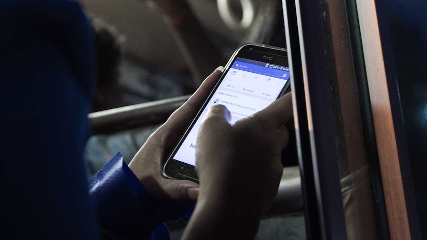 A young woman looks at her Facebook wall while she travels on a bus in Yangon.