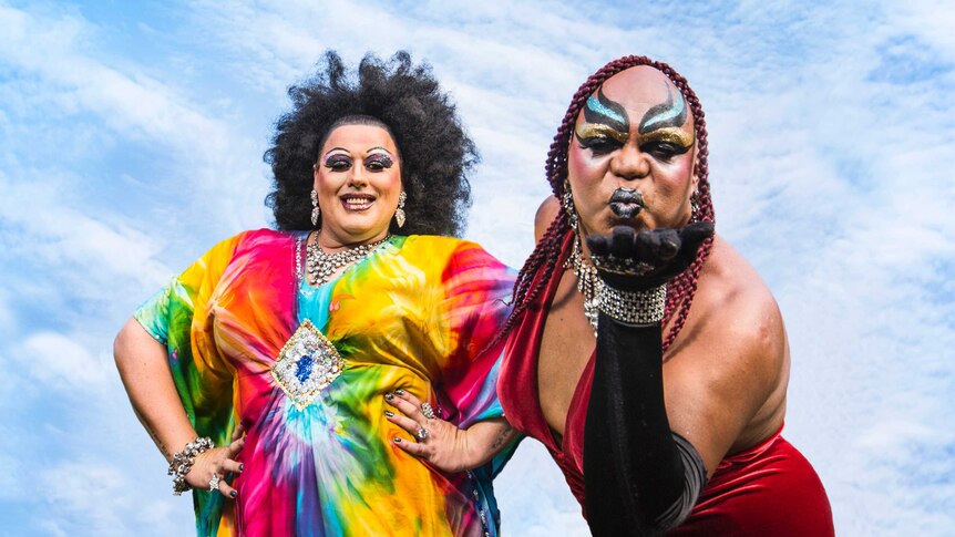 Colour photograph of Lasey Dunaman and Nova Gina of drag act Dreamtime Divas posing with a blue cloudy sky behind them.