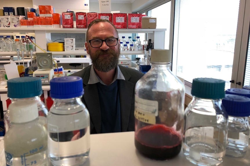 A man looks at the camera with bottles of medicine surrounding him.