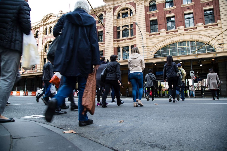 People walk across the street towards Flinders Street Station.