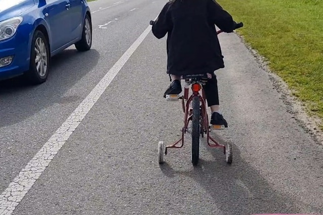a child riding their bike along the side of the road near a car.
