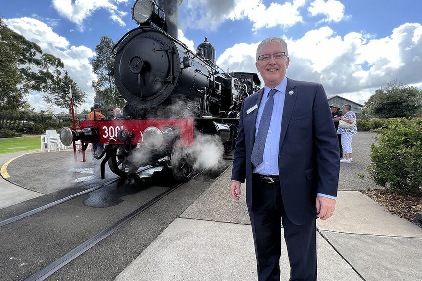 A man in a suit stands before a steam train