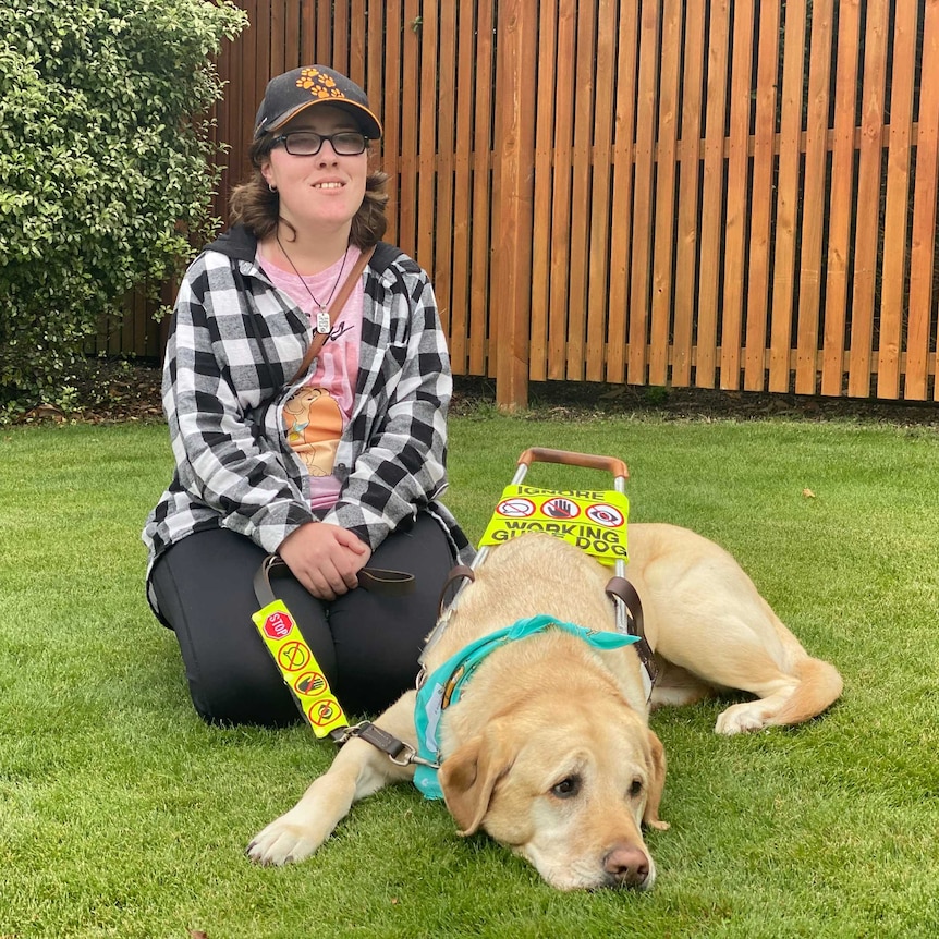 A young woman in a checked shirt and cap with a guide dog.