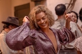 Margot Robbie wears purple dress and smiles while dancing in still from movie Babylon