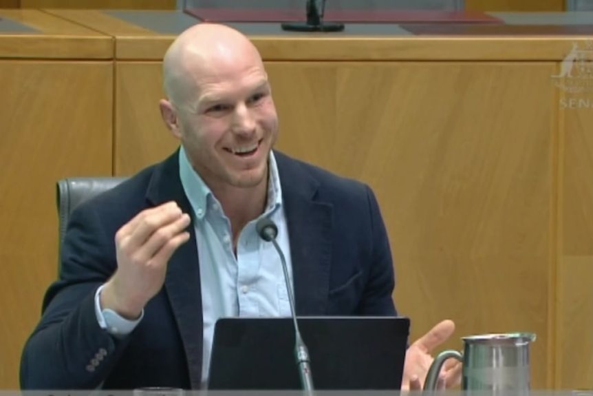 A man speaks, smiling at a committee.