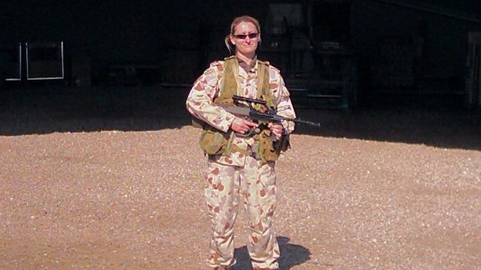 Tara Young wearing her service uniform, which is camouflage print, and carrying a gun.