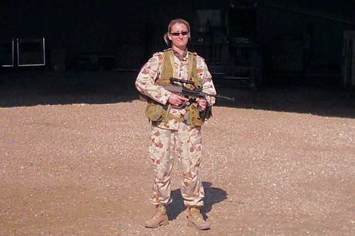Tara Young wearing her service uniform, which is camouflage print, and carrying a gun.