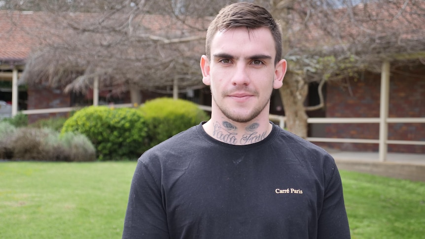 man with tattoos on neck in black shirt looks seriously at camera