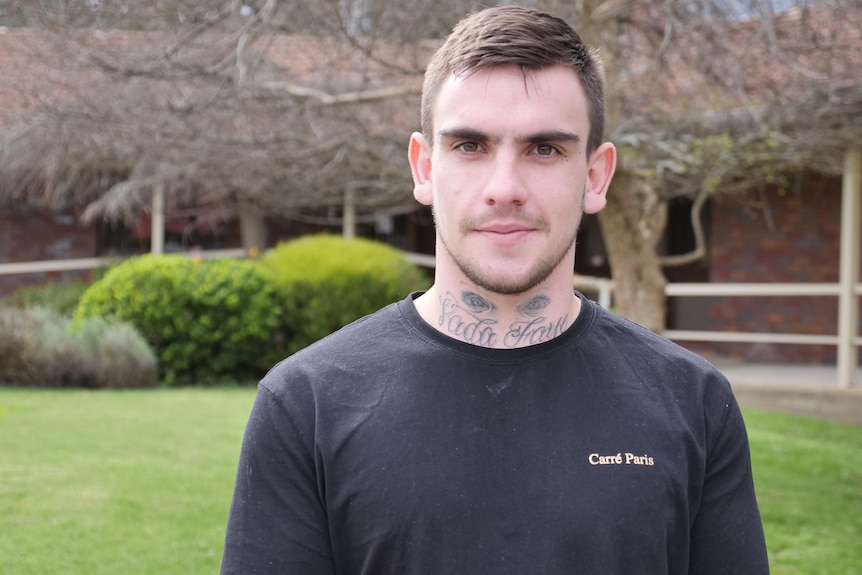 man with tattoos on neck in black shirt looks seriously at camera