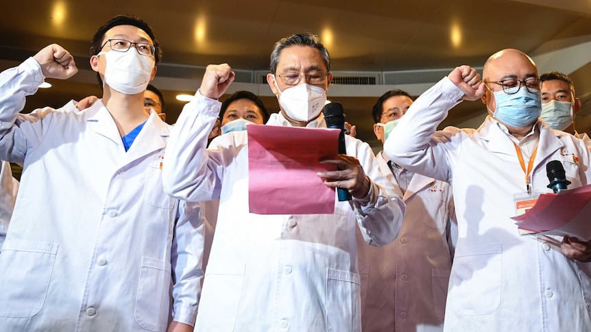 Three Chinese doctors in face masks with their fists in the air