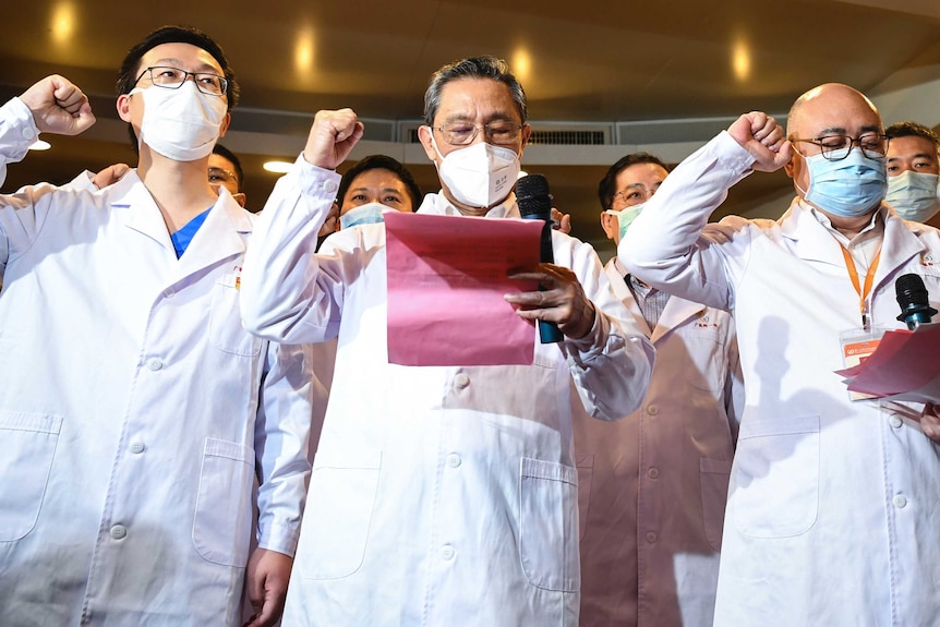 Three Chinese doctors in face masks with their fists in the air