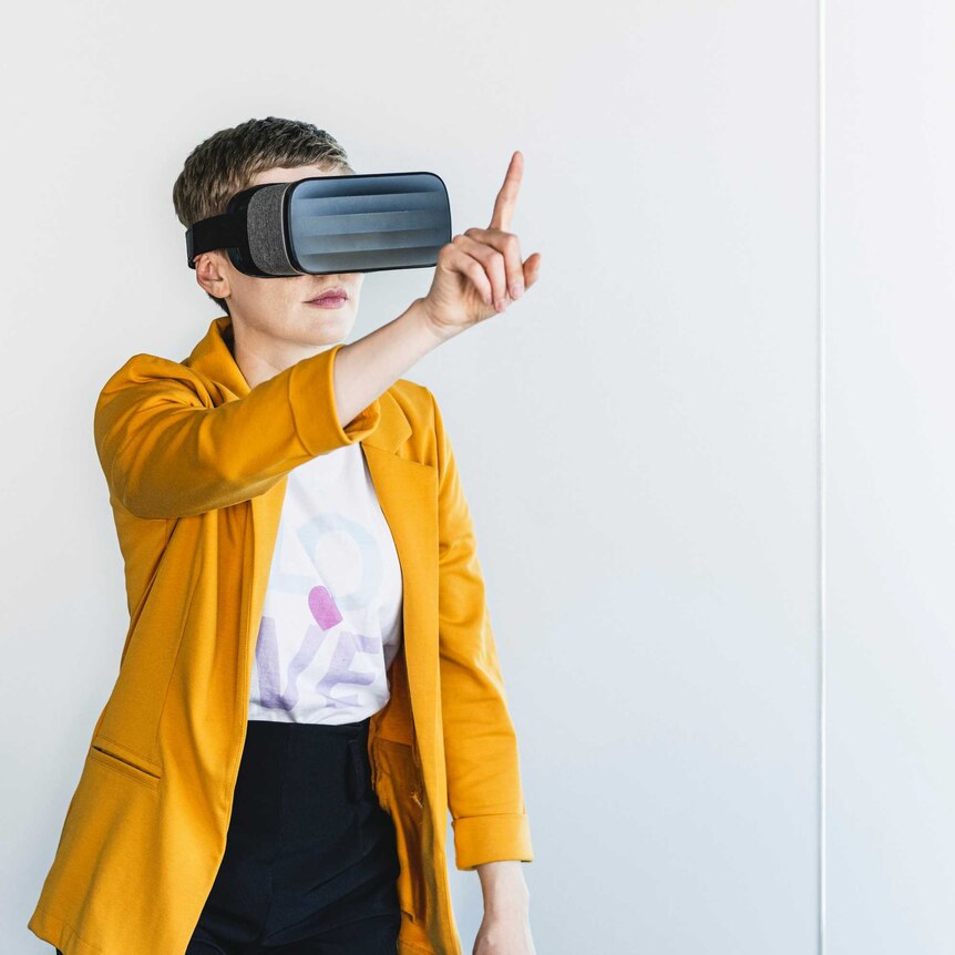 Businesswoman wearing blazer looking through virtual reality simulator while standing against wall in office
