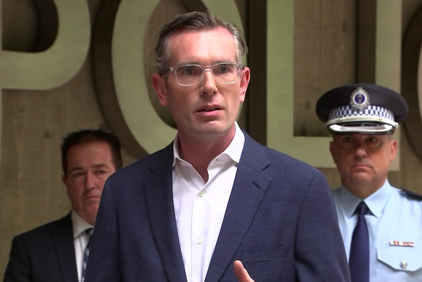 a man wearing glasses standing outdoors talking to the media