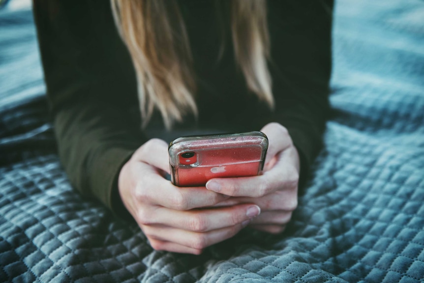 An unidentifiable woman with long hair holds a red iPhone.