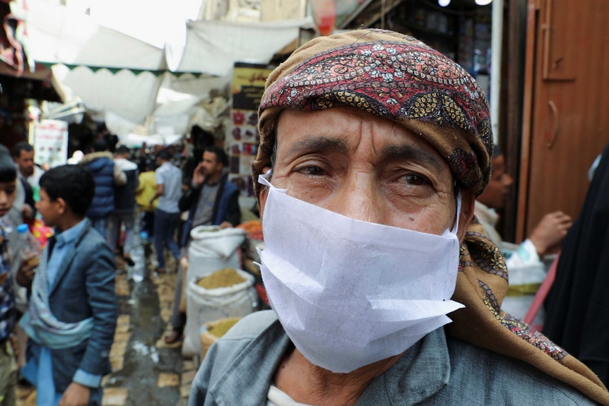 A man wears a protective face mask at a crowded street market.