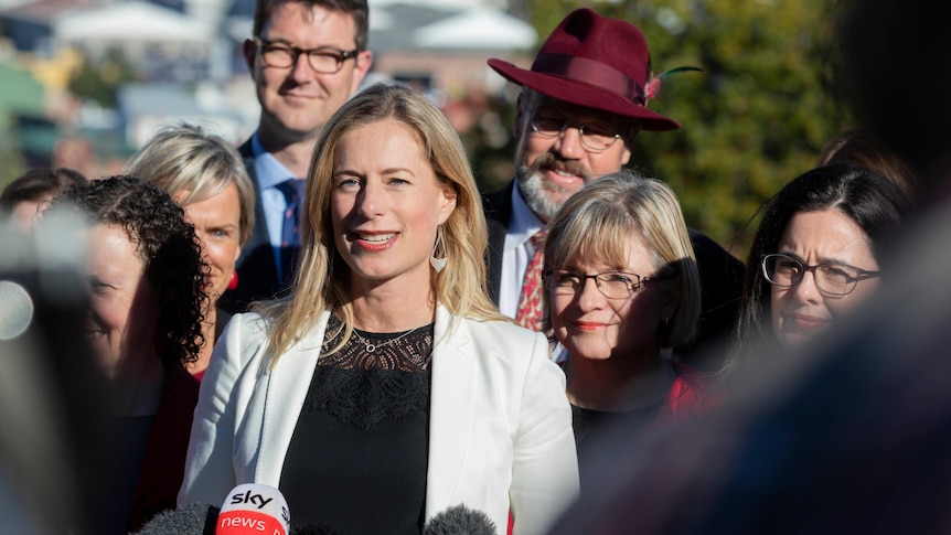 A woman in a white blazer is in the centre of a group of smiling peopkle