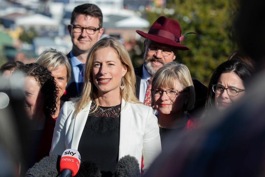 A woman in a white blazer is in the centre of a group of smiling peopkle