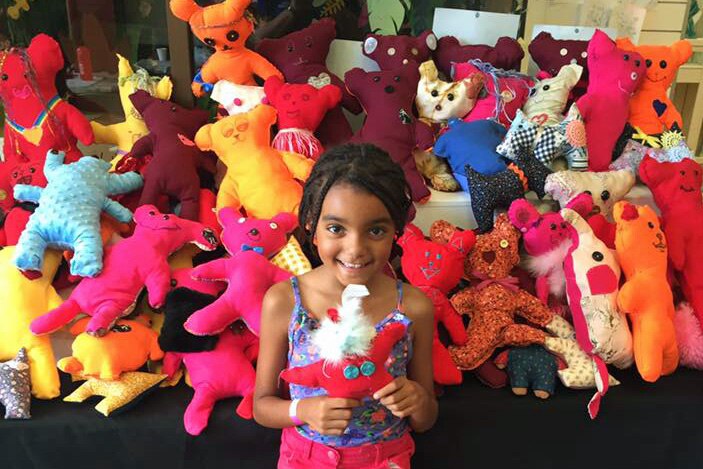 Young girl stands with brightly coloured handmade bears.