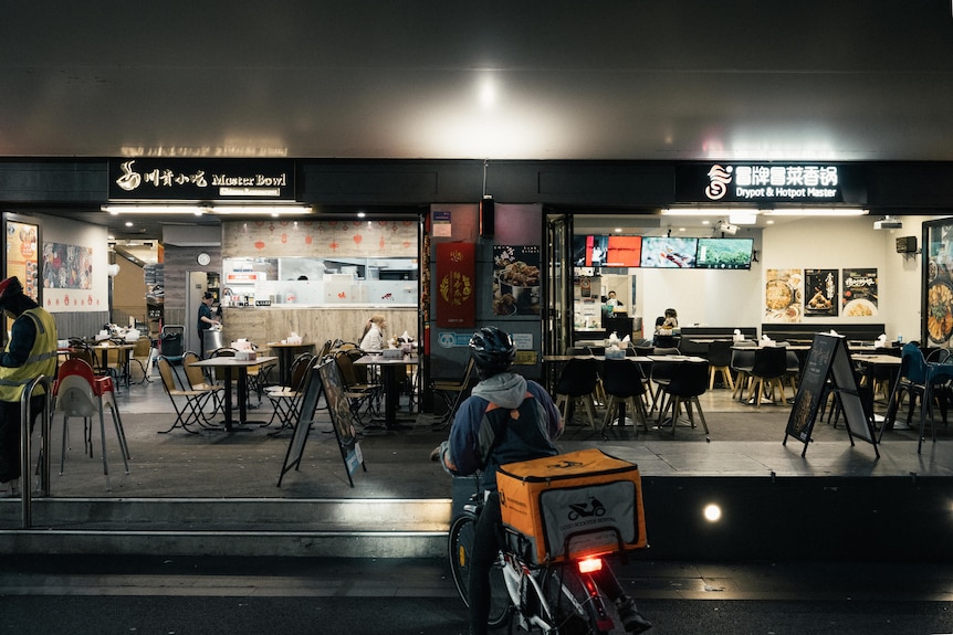 A photo of a delivery man and bike waiting in front of a restaurant at night in Sydney's Chinatown.