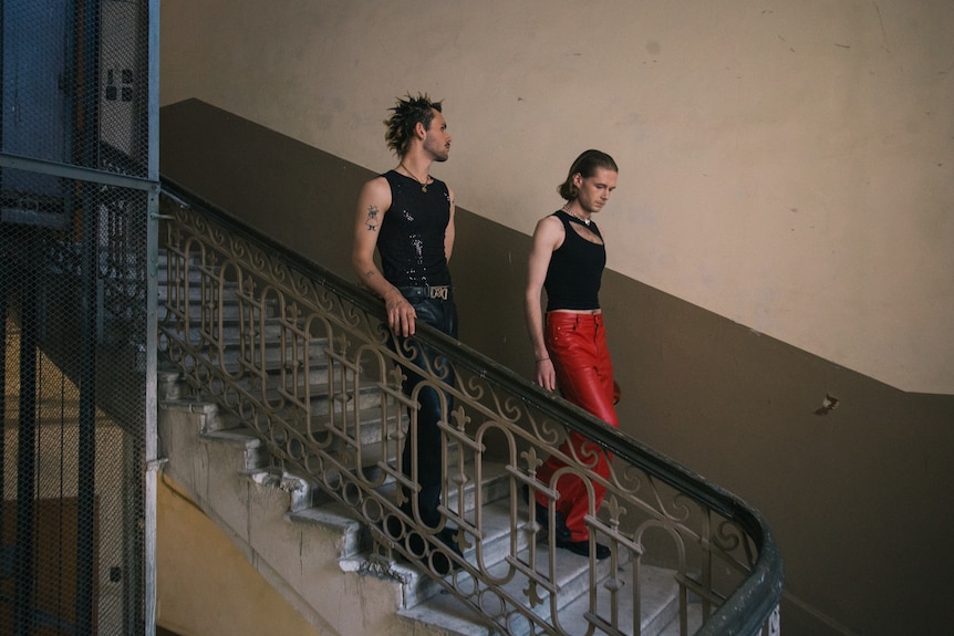 Two queer men walk down a flight of stairs in an apartment block. 