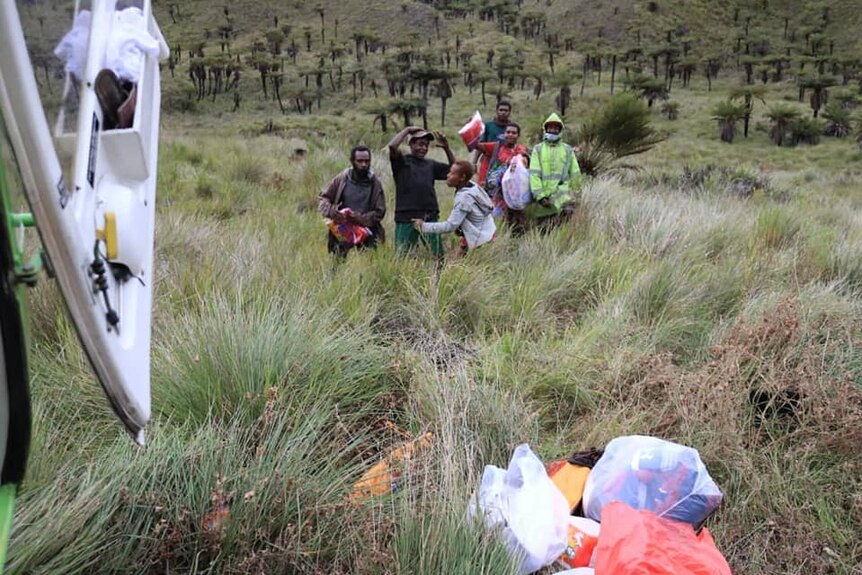 A group of people stand on a mountainside as seen from inside a helicopter.