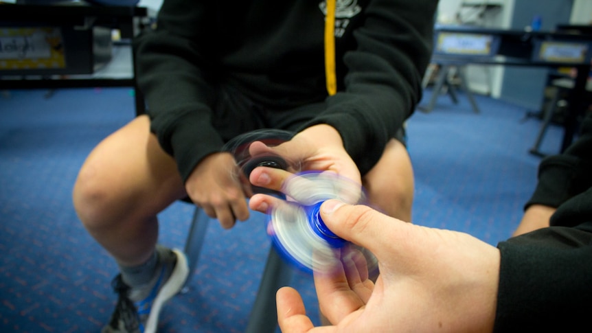 Fidget spinner in hands of children sitting in classroom.