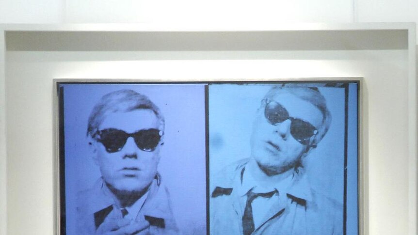 A Christie's employee stands next to Andy Warhol's Self-Portrait