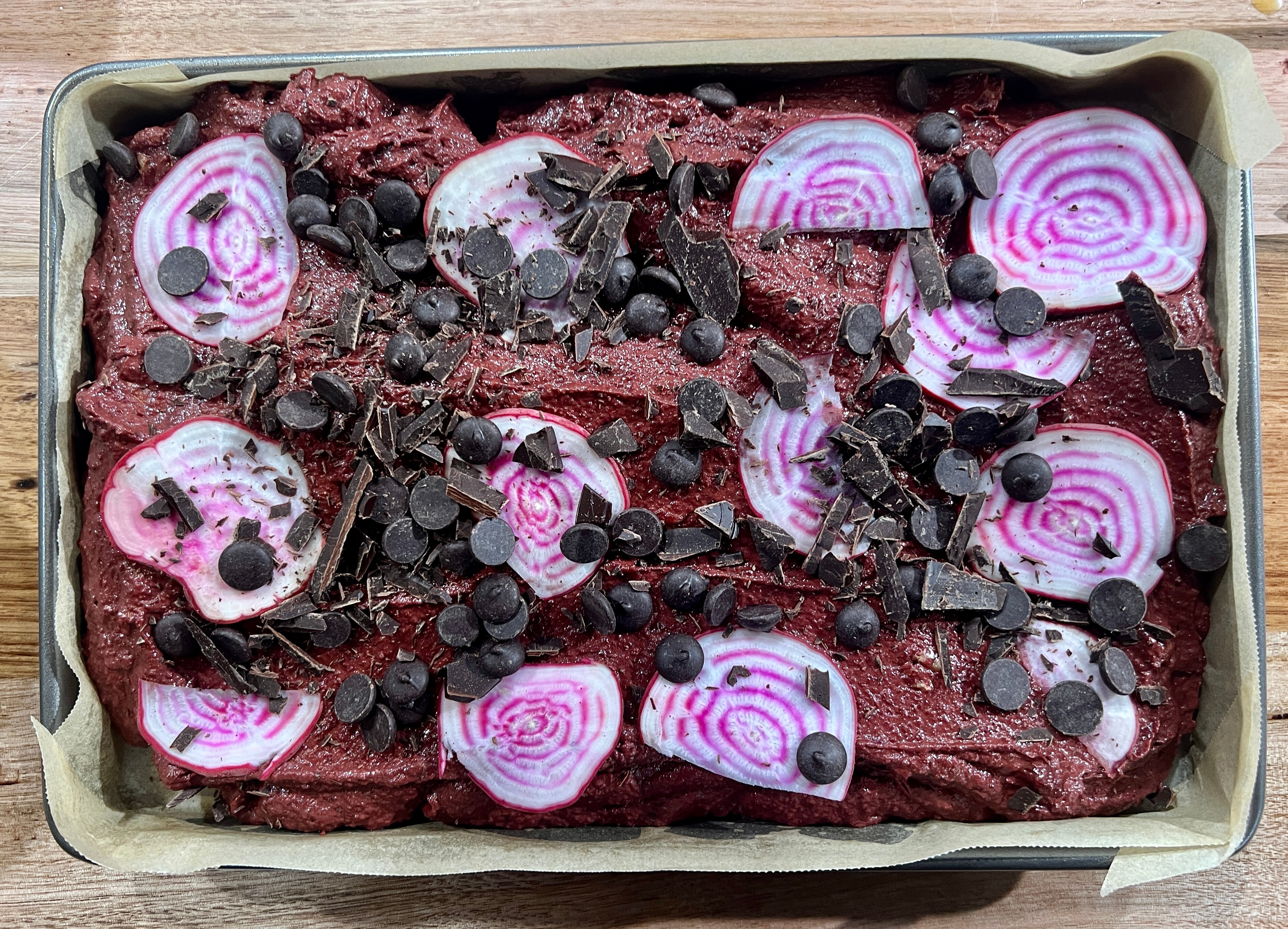 orange and beetroot brownie mix in baking tray with choc bits and parsnip on top ready to be put in oven
