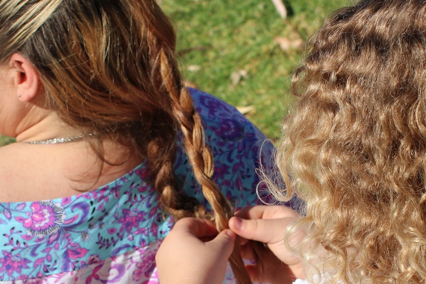 A girl plaits a woman's hair.