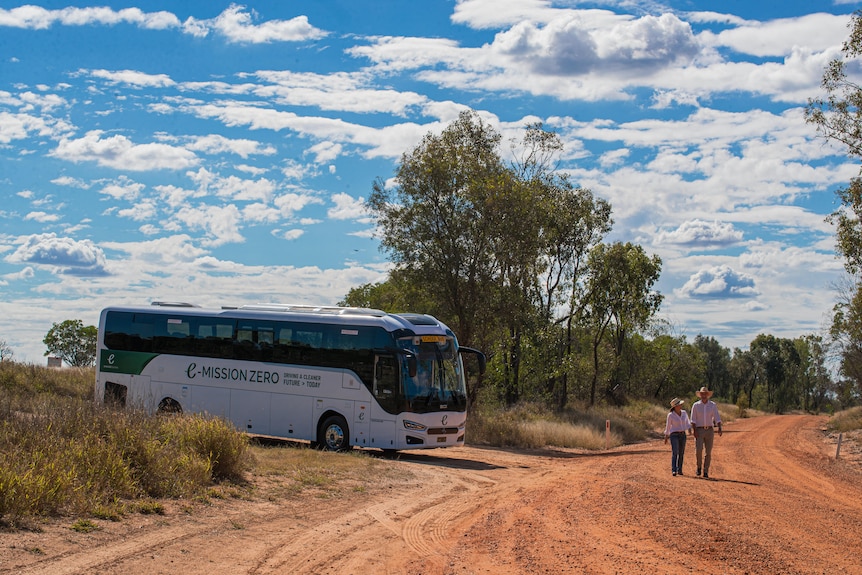 Un homme et une femme sur une route poussiéreuse avec un bus en arrière-plan