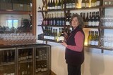 A woman stands holding a bottle of wine in a vineyard's cellar door 