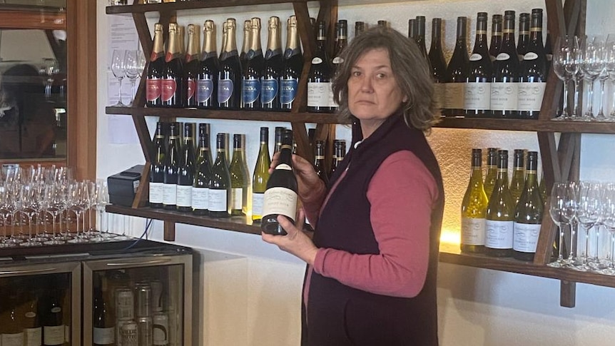 A woman stands holding a bottle of wine in a vineyard's cellar door 