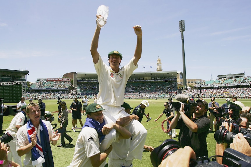 Australian cricketer Glenn McGrath holds a glass trophy as two Australian teammates hold him on their shoulders at the SCG. 