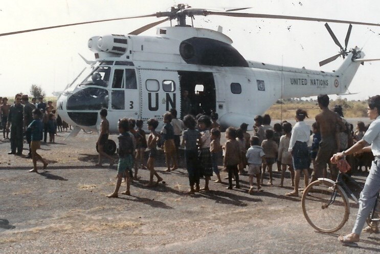 A big white United Nations helicopter resting on the ground, surrounded by Cambodian children.